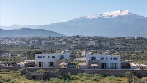 A modern building with a flat roof, large windows, and a patio area with outdoor seating. - Elysioum Pearl Villas - With 2 Private Pools (Mylopotamos)