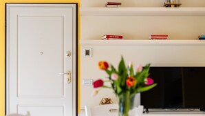 Een kamer met een witte deur, een witte tafel met een bloevas en een plank met boeken en decoratieve objecten.