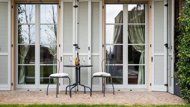 Een terras met een tafel, stoelen, een schuifdeur en een vloer van natuursteen.
