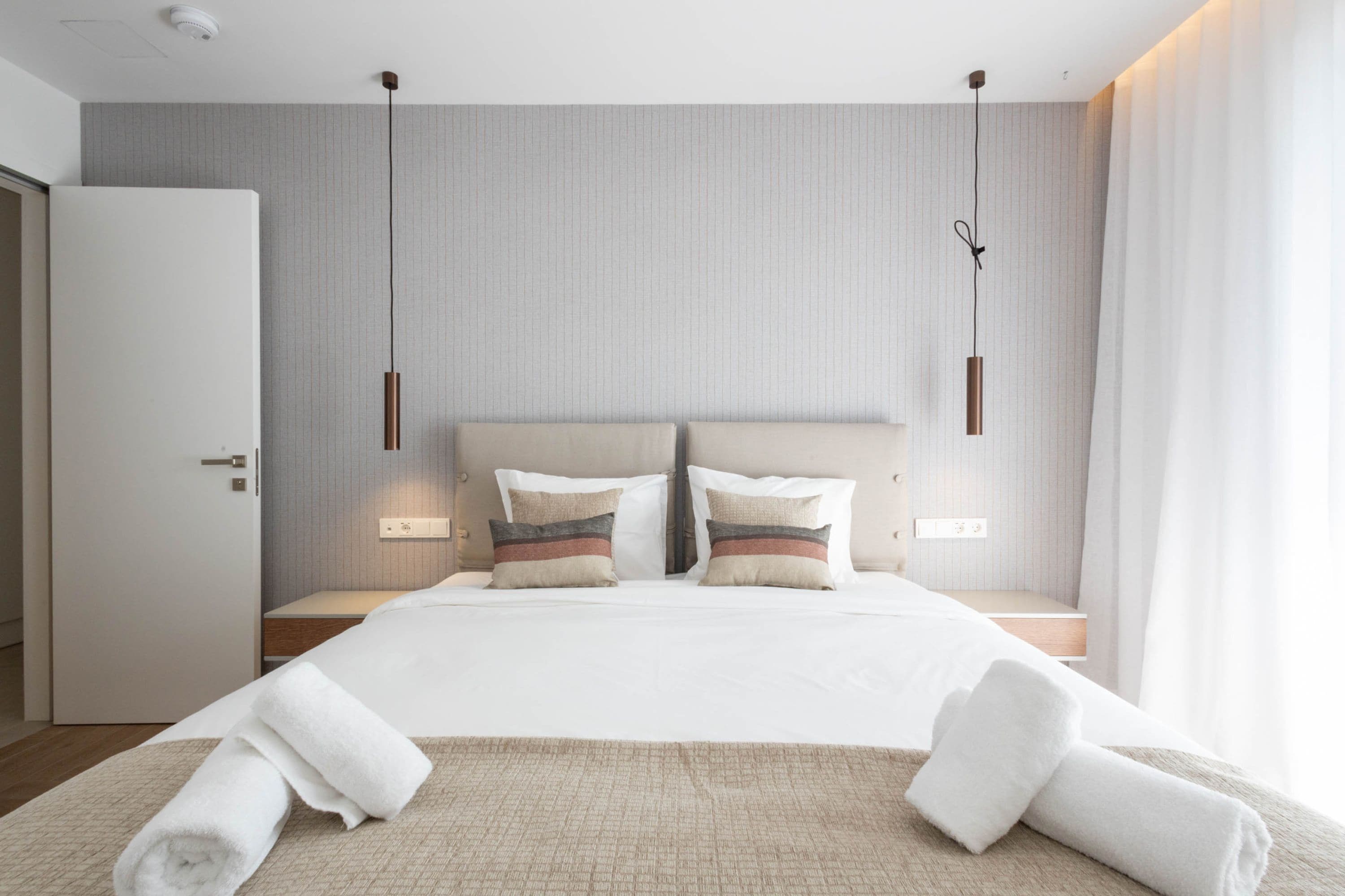 A modern hotel room with a large bed, two bedside tables, a headboard, and a window with curtains.