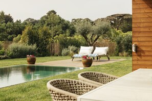 A poolside area with wicker chairs, a lounge chair, and a wooden deck. - Moon Forest Retreat by Cadenzalux (Sintra)