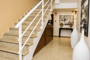 A staircase with white railings leading to a landing, a reception desk, and a wall with framed artwork.