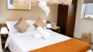 A neatly made bed with white and brown pillows, a rolled white towel, and an orange textured throw blanket.