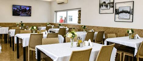 A restaurant with multiple tables, wicker chairs, and white tablecloths.