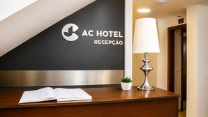 A hotel reception desk with a black wall, a logo, and a lamp.