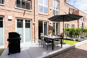 A patio with a grill, outdoor table, chairs, and an umbrella. - MeerNah love. Terrace. Close to the beach. Infrared cabin. (Grömitz)