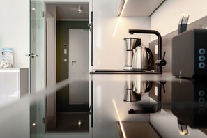 A modern kitchen with a built-in espresso machine, a glass door leading to a room, and a white cabinet with a milk carton. - MeerNah love. Terrace. Close to the beach. Infrared cabin. (Grömitz)