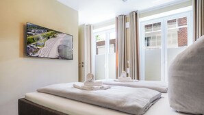 Una camera d'albergo con un letto, una finestra con tende, una TV a muro e vista su una ruota panoramica.