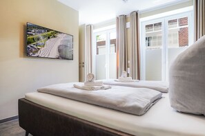 Ein Hotelzimmer mit Bett, einem Vorhangfenster, einem an der Wand montierten Fernseher und Blick auf ein Riesenrad.