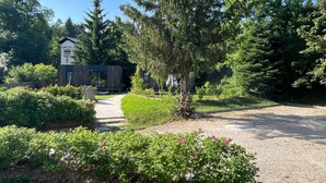 A pathway leading to a modern building with a wooden exterior, surrounded by lush greenery and flowering bushes. - Tiny House near Forstsee – Nature, Tranquility & Lakes (Greilitz)