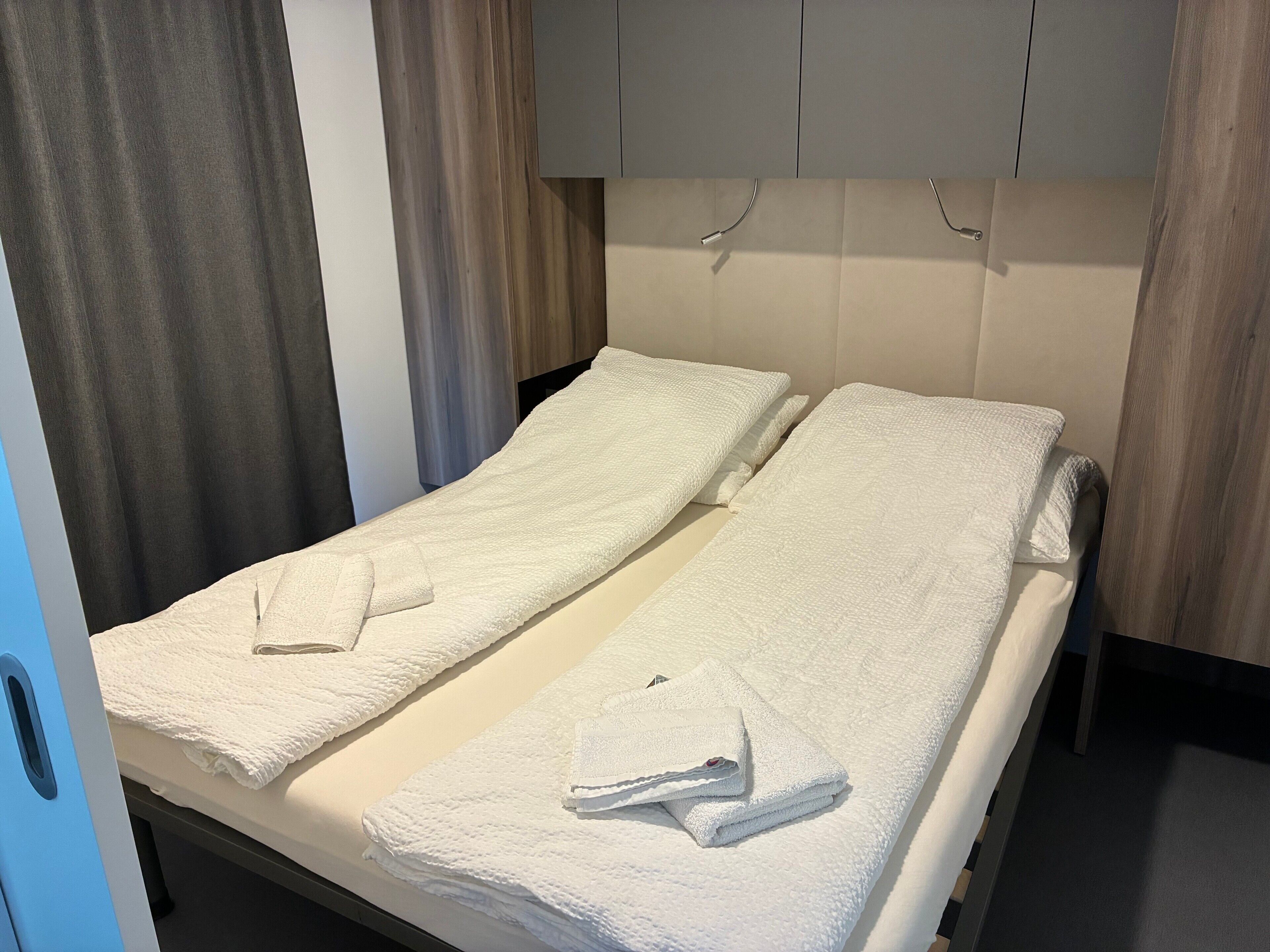 A hotel room with a bed, two towels, a curtain, and a wooden headboard.