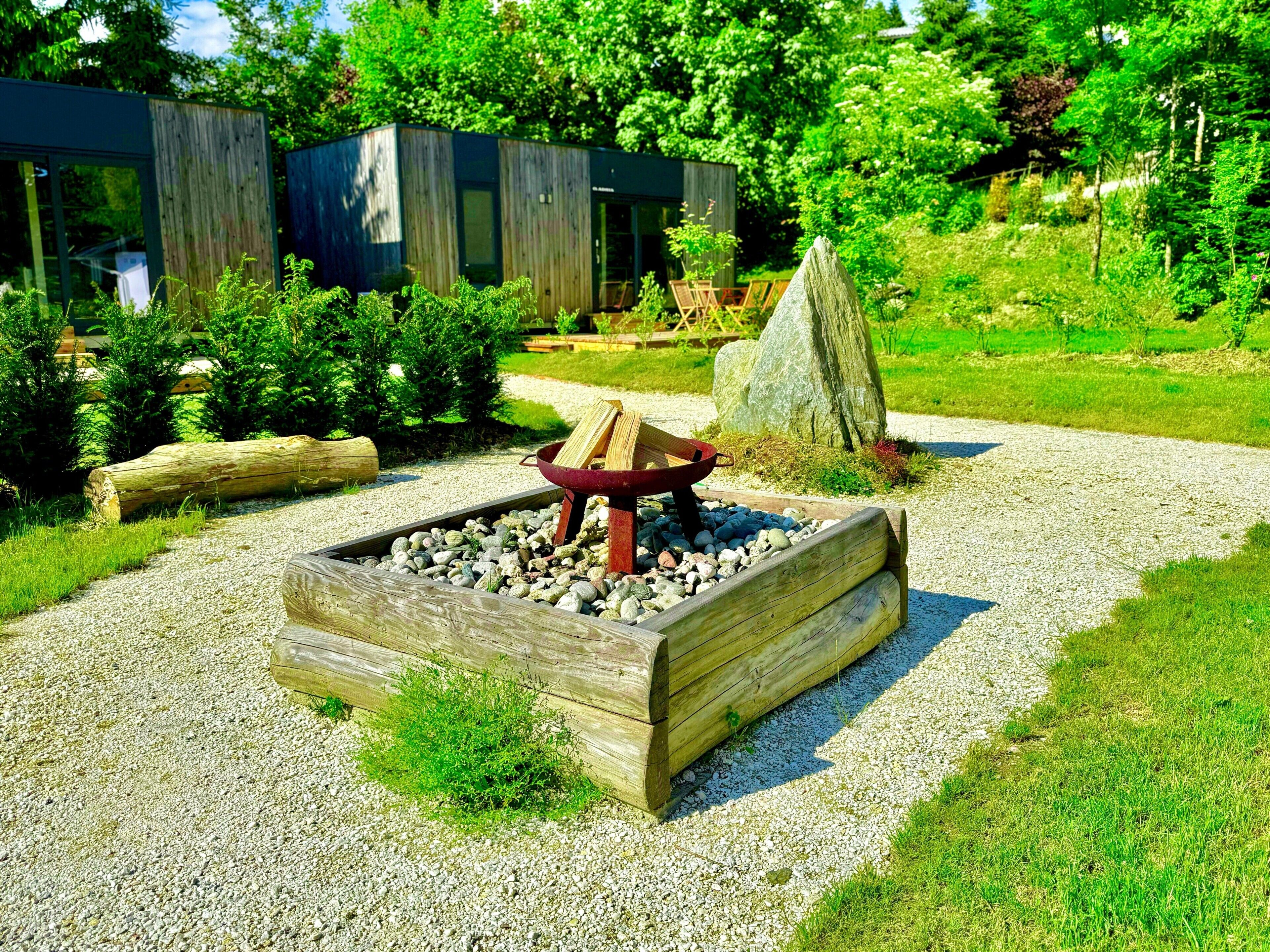 Een modern buiten vuurplaatsgedeelte met een houten constructie, omringd door grind en groen.