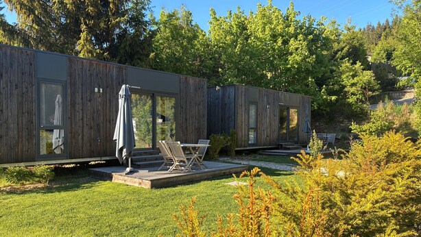 A wooden cabin with a deck, outdoor seating, and a view of surrounding trees. - Tiny House near Forstsee – Nature, Tranquility & Lakes (Greilitz)