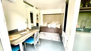 A compact room with a bed, a small table with a bottle, a chair, and a sink. - Tiny House near Forstsee – Nature, Tranquility & Lakes (Greilitz)