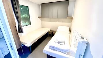 A compact hotel room with a single bed, a small bedside table, a desk, and a window with curtains.