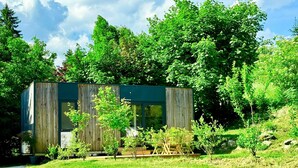 A modern wooden cabin with a glass front, surrounded by lush greenery and trees. - Tiny House near Forstsee – Nature, Tranquility & Lakes (Greilitz)