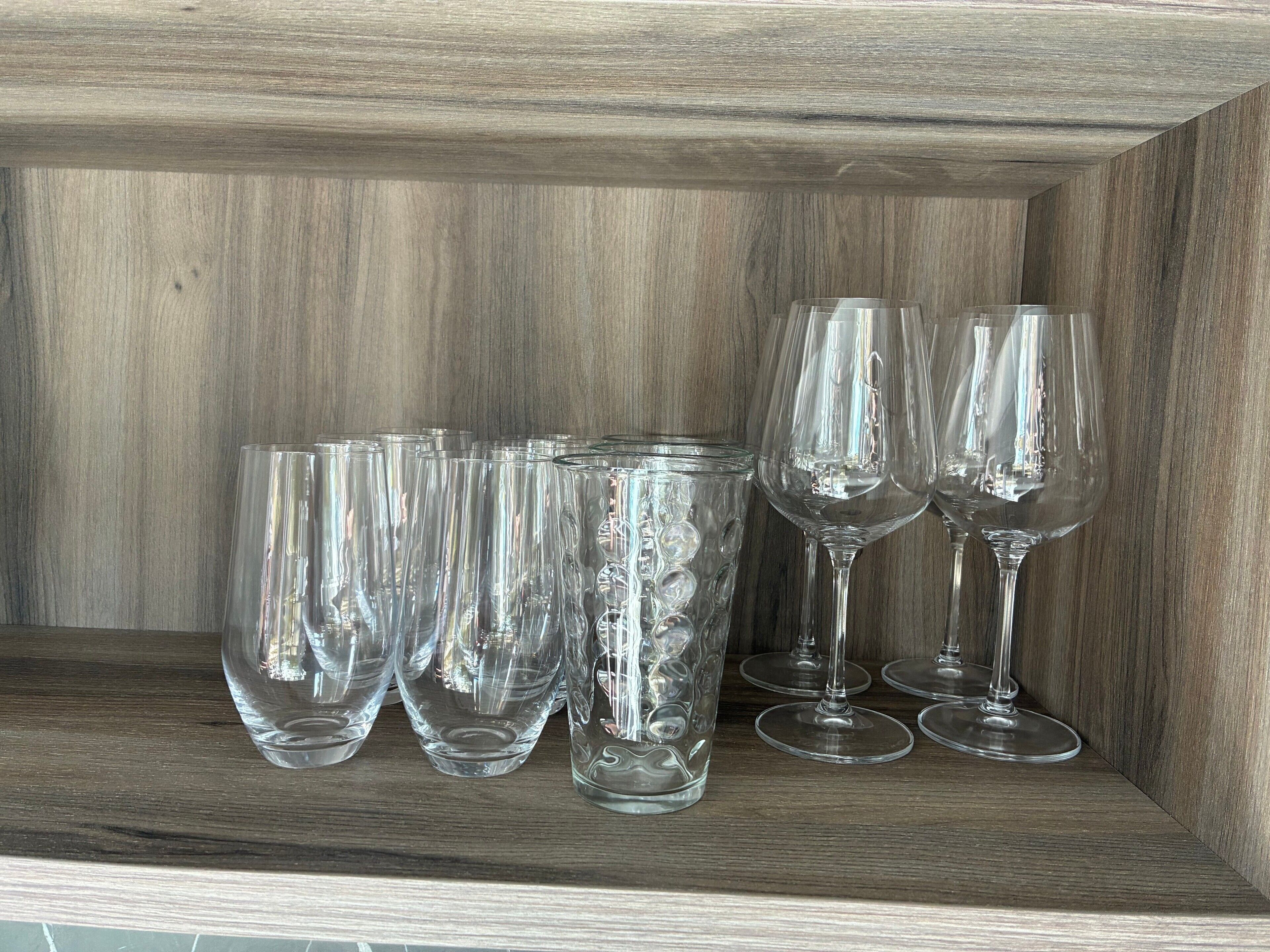 A wooden shelf with several clear glass wine glasses and tumblers.