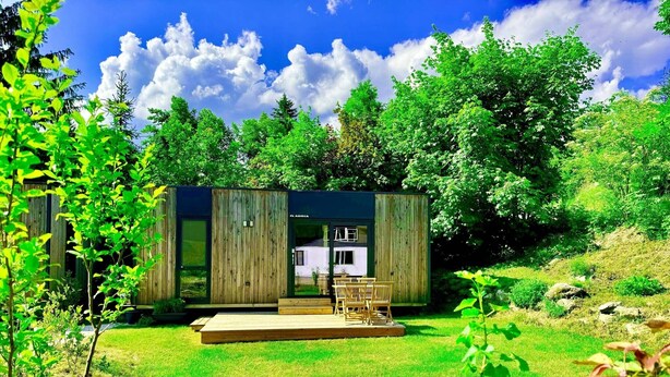 Une cabane en bois moderne dotée d’une porte en verre, d’une terrasse et d’une cour gazonnée.