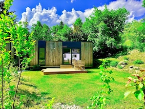 Una cabaña moderna de madera con puerta de cristal, un balcón y un patio con césped.