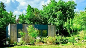 Un bâtiment moderne à l’extérieur en bois, entouré d’une végétation luxuriante et bordé d’un chemin de gravier.