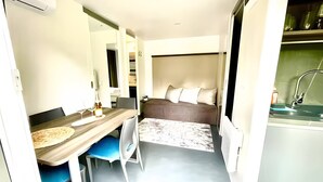 Une chambre d’hôtel de taille réduite comprenant un lit, un petit bureau avec une chaise, une table à manger et un coin cuisine.