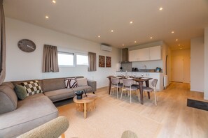 A modern living room with a sofa, coffee table, and dining area with chairs. - Enjoy stylish comfort in the Duinrand Lodge for 6 persons. This cozy and spacious holiday home offers everything you need for a truly relaxing holiday. (De Haan)