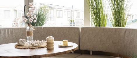 A corner seating area with a round table, a vase with flowers, and a cake on a plate.