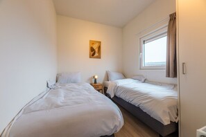 Un dormitorio con dos camas, una mesita de noche con lámpara, una ventana con cortinas y una obra de arte en la pared.