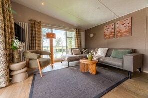 A modern living room with a sofa, a chair, a coffee table, and a TV. - Experience the Strandrust Lodge at Holiday Park Blankenberger Duinen at any time of the year. Enjoy a carefree holiday with the whole family. (De Haan)