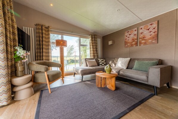 A modern living room with a sofa, a chair, a coffee table, and a TV. - Experience the Strandrust Lodge at Holiday Park Blankenberger Duinen at any time of the year. Enjoy a carefree holiday with the whole family. (De Haan)