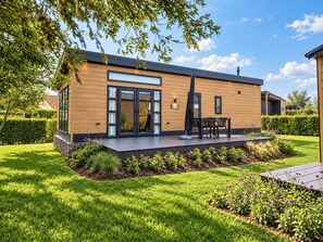 A modern two-story house with a deck, surrounded by a well-maintained garden and a clear sky. - Experience the Strandrust Lodge at Holiday Park Blankenberger Duinen at any time of the year. Enjoy a carefree holiday with the whole family. (De Haan)
