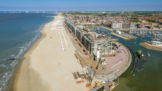 Luchtbeeld van een kuststad met een strand, jachthaven en hoge woontorens.