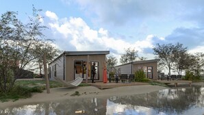 Een modern gebouw met een overdekt buitengebied, een hangmat en een waterpartij.