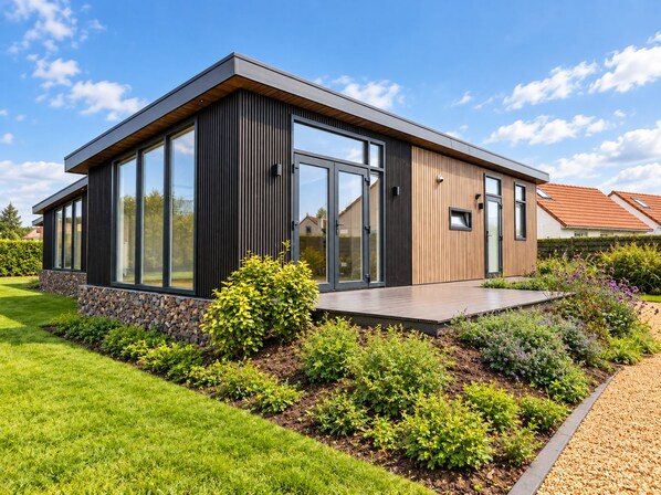 Et moderne hus med store vinduer, en træterrasse og en velplejet have.