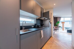 A modern kitchen with grey cabinets, a stainless steel sink, and a window overlooking a balcony. - The Havenlicht Lodge is a comfortable holiday home for 4 persons, featuring modern amenities and a private terrace on the Flemish coast. (De Haan)