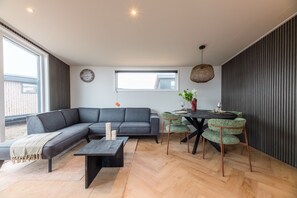 Ein moderner Wohnraum mit einer Eckcouch, einem Esstisch mit Stühlen, einem Couchtisch und einem großen Fenster, das für natürliches Licht sorgt.