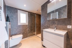 Et moderne badeværelse med toilet, vask og brusekabine i glas.
