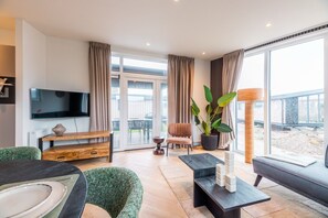 A modern living room with a flat-screen TV, a wooden bench, a sofa, and a dining table. - The Havenlicht Lodge is a comfortable holiday home for 4 persons, featuring modern amenities and a private terrace on the Flemish coast. (De Haan)