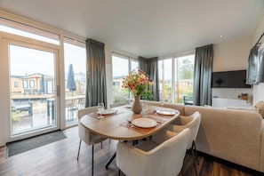 Ein modernes Esszimmer mit einem Holztisch, gedeckt für vier Personen, einer Couch und Blick ins Freie.
