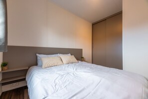 A modern bedroom with a bed, built-in shelving, and a wardrobe. - In the Duinrand Lodge for 4 persons, you can truly relax. This comfortable and tastefully furnished holiday home guarantees pure holiday enjoyment. (De Haan)