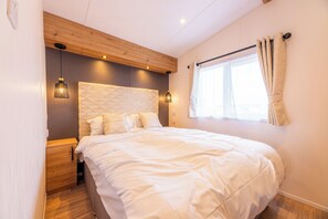 A modern bedroom with a large bed, wooden headboard, bedside lamps, and a window with curtains. - Enjoy your holiday in the Zeebries Cabin: a comfortable holiday home on the Flemish coast for 4 persons, fully equipped for a carefree stay. (De Haan)