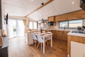 A modern kitchen with wooden cabinets, a dining area with a white table and chairs, and a large window providing natural light.