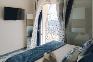 Ein Schlafzimmer mit Bett, Fernseher, Fenster mit Vorhängen und einem gemusterten Boden.