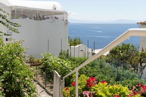 Ein weißes Gebäude mit Meerblick, ein Balkon mit Geländer und ein Garten mit rosa Blumen.