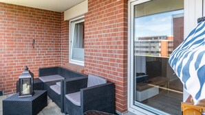 A balcony with wicker furniture, a lantern, and a sliding glass door. - Apartment 'Fewo Strandweh in Dornumersiel' with Balcony and Wi-Fi (Dornum)