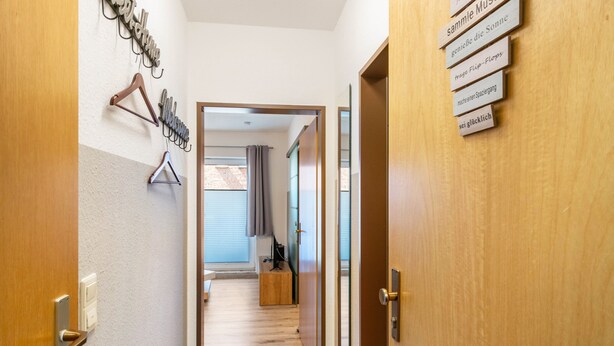 A hallway with wooden doors, a coat rack, and a sign with text. - Apartment 'Fewo Strandweh in Dornumersiel' with Balcony and Wi-Fi (Dornum)