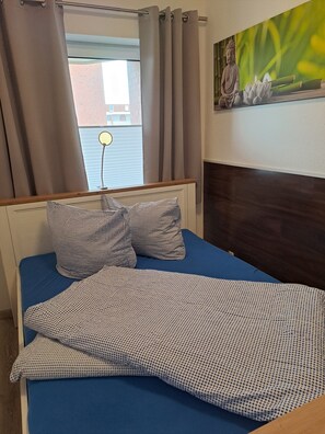 Ein Bett mit blauer Matratze, karierten Kissen und einer gemusterten Decke.