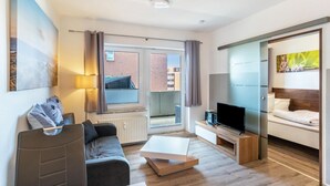 A modern living room with a sofa, coffee table, TV, and artwork on the wall. - Apartment 'Fewo Strandweh in Dornumersiel' with Balcony and Wi-Fi (Dornum)
