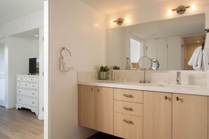 A bathroom with a large mirror, two sinks, wooden cabinets, and a towel rack. - Wailea Elua | Steps to Ulua Beach, Ocean Views (Wailea-Makena)