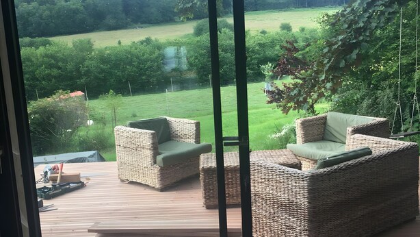 Quarto com uma grande porta de vidro deslizante que dá para um pátio externo com móveis de vime e vista para uma paisagem verde.